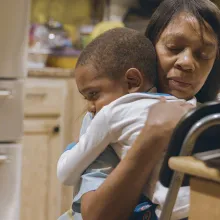 A Black woman is holding a toddler