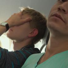 Two Russian man are in their plane seats, one person with a hand cover his face