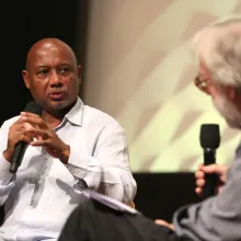 Raoul Peck speaking into the mic facing with Kenneth Turan