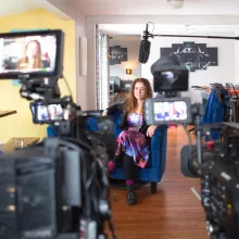 Woman in a galaxy-themed dress sits in an interview set up before a documentary crew