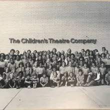 A black and white class photo in front of a building named "The Children's Theater Company"