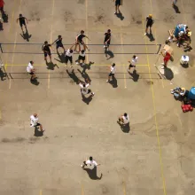 We look down from above at a  crowd of Asian-American men playing street volleyball.