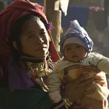 An Asian woman in an elaborate headscarf and necklaces holds her infant child.