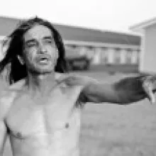 Black and white photograph of a shirtless Native American man reaching his arm out in mid-speech