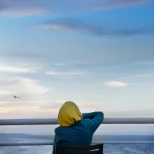 An individual in a yellow hijab sits in a chair in the stern of a boat before the ocean