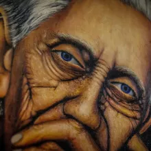 A close-up of a painting of a wrinkled face of an old woman.