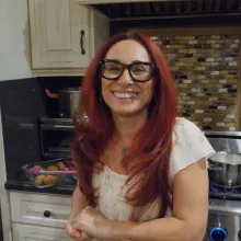 A red-haired Armenian-American smiles at the camera in a home kitchen.