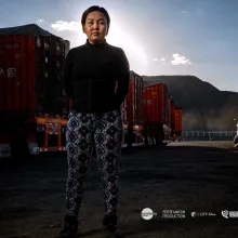 woman stands in front of trucks, mountains in the background