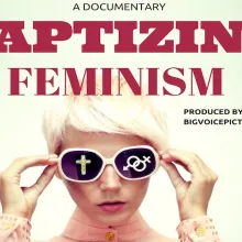 A young Caucasian woman with a pixie cut adjusts her black sunglasses with white frame. There is a cross symbol in her left sunglass shade and gender symbols in the right sunglass shade. 