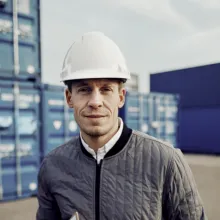 A port worker standing in front of several blue ship crates.