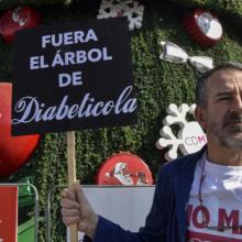 A Mexican activist stands in front of a Christmas tree with a sign.