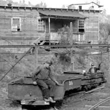 Early 20th century West Virginian miners sit on mine carts outside of a wooden house.