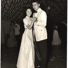 Mary and Kelly Adachi smile and slow dance in their wedding outfits. 