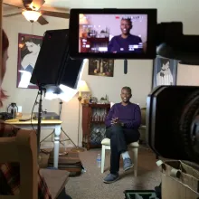 A queer black elder sits with their legs crossed during an interview in their mid-sized artistically decorated Living Room