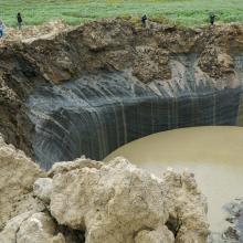 group of people stare into sink hole cause by underground methane explosions