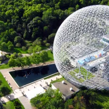 A geometric steel dome sits on a green landscape. 