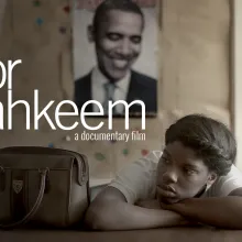 main character Daje rests her head on crossed arms at desk with bookbag and photo of Obama behind on wall