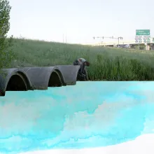 young boy sitting on top of one of three drainage tunnels expelling blue water color paint