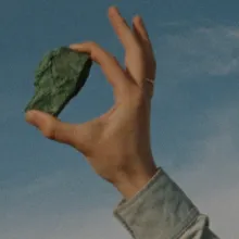 A rock held up to the sky between the index and thumb of a masculine hand