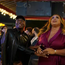 New Orleans city council candidate Mariah Moore, a Black Trans woman, wears a burgundy dress. She smiles and holds her brother's hand in anticipation of the incoming election results. 