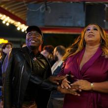 New Orleans city council candidate Mariah Moore, a Black Trans woman, wears a burgundy dress. She smiles and holds her brother's hand in anticipation of the incoming election results. 