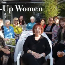 Thirteen elderly White  women sit around a white patio table facing the camera. 