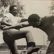 A black and white photo of two African-American man showcasing their stunts.