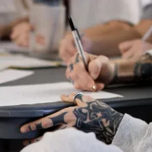 the tattooed hands of an inmate fill out paperwork.