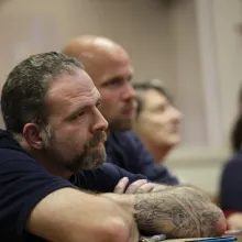 middle aged white male convict listens with arms crossed at a re-entry training