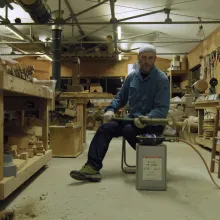 Man sits in a craft workshop with a bamboo flame over a controlled flame.