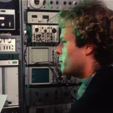 Ken Kelley stares in profile, surrounded by towers of sound recording equipment. 