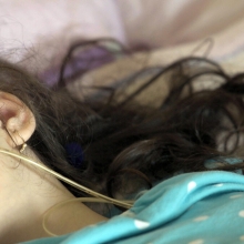 A girl with dark brown hair is lying on the bed, being nourished via feeding tube