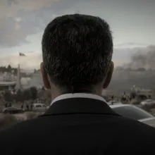 Main subject of film looks away from camera towards his town in a suit.