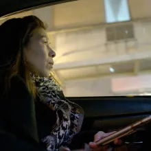 Chinese-American woman holds her phone in her hand while staring out the window of a taxi cab.