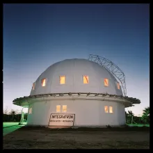 A white dome research center sits on a green lawn at dusk with stars shining in the sky above