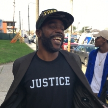 Black male smiles at bystanders as he shows his t-shirt with the word "Justice" on it.