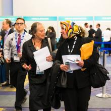 Two women are talking while walking away from a booth in a conference.