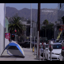 The tent of an unhoused person on the street with the hollywood sign in the background.