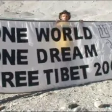 three men in orange jackets hold a banner which reads "one world, one dream, free Tibet 2008"