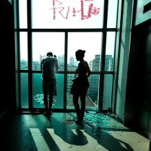 2 people inside a high-rise, standing next to an elevator. The window's glass is shattered.