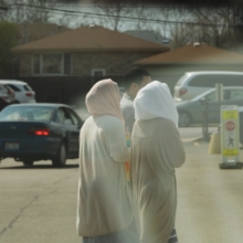 two women dressed in traditional muslim attire walk through parking lot with male 