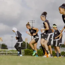 female football team runs laps on a green field in black uniforms