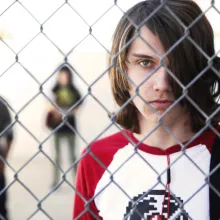 white male teen looks through chainlink fence at school