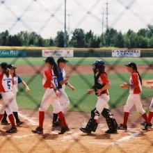 opposing female baseball teams high five in the baseball field at the end of the game.