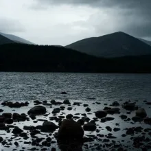 The rocky shore of a large body of water with mountains beyond.