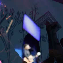 abstract superimposed image of fans raising their hands and a man playing guitar on stage.