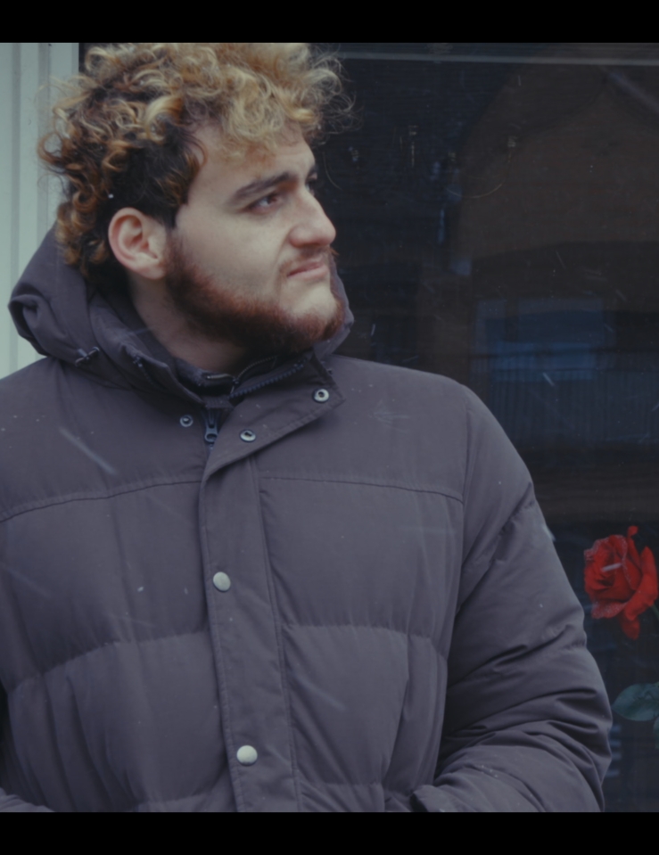 A young man wearing a puffy jacket looks to the side.