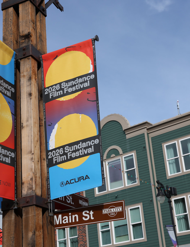Street lamp posters advertising the 2026 Sundance Film Festival with a view of Main Street buildings against a bright blue sky