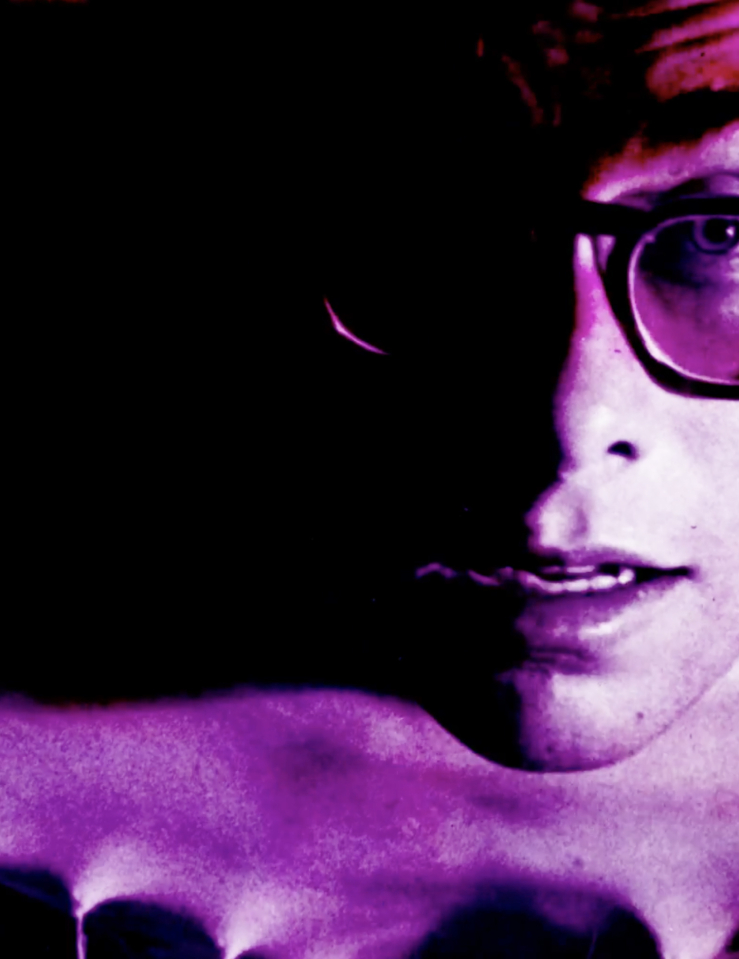 A magenta-tinted image of a man with glasses, leaning forward.