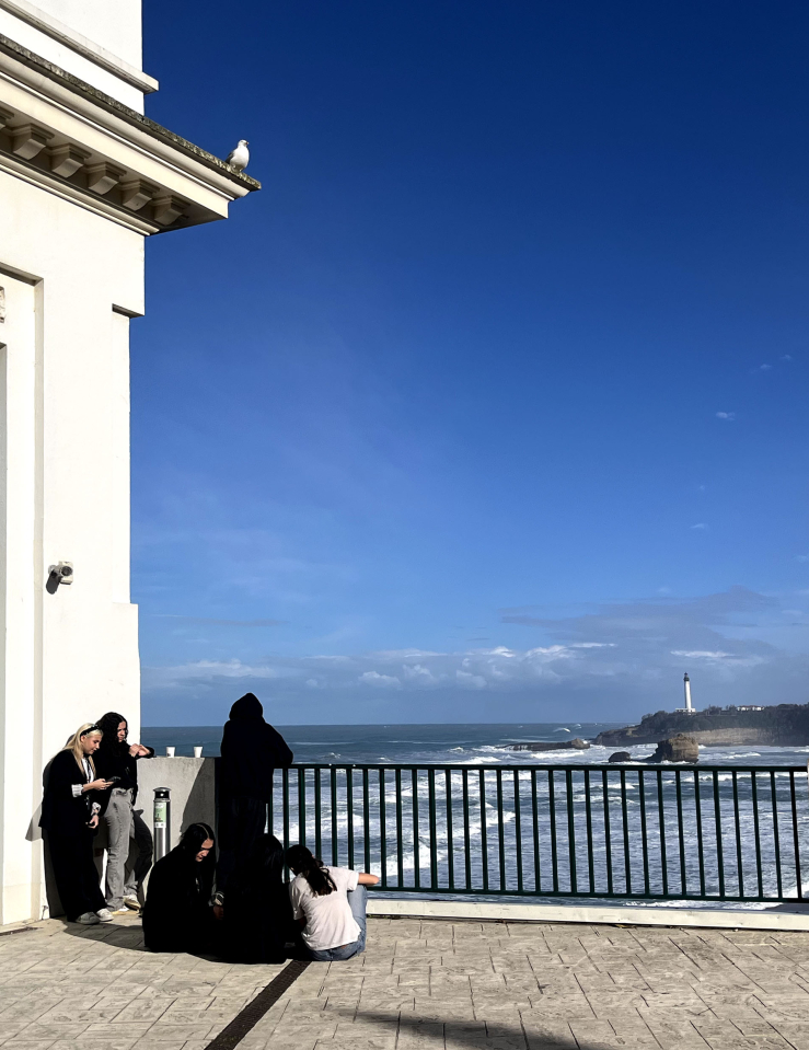 Overlooking crashing waves, a small group of people relax in front of a FIPADOC poster.